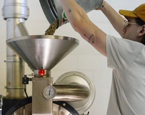 Person pouring coffee beans into a coffee roaster.