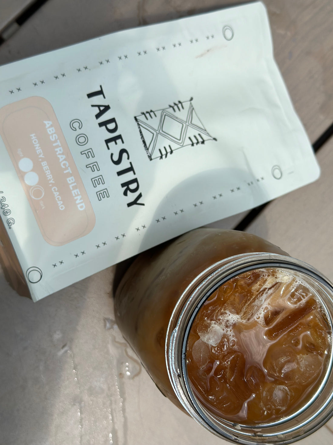 12 oz bag of tapestry coffee abstract blend on wood table with glass of iced coffee